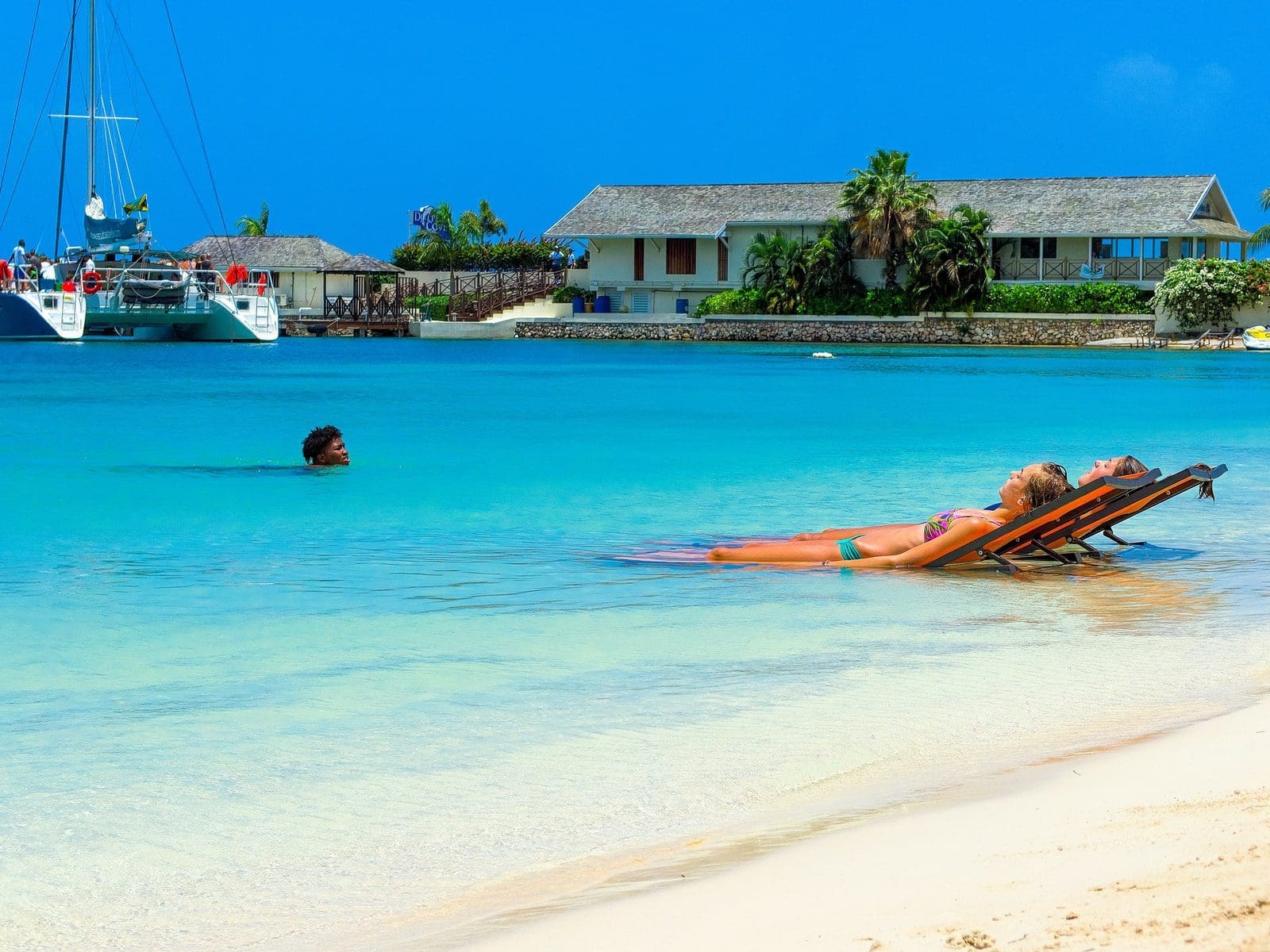 investing in precious metals two women sun bathing and another man swimming on blue body of water during daytime