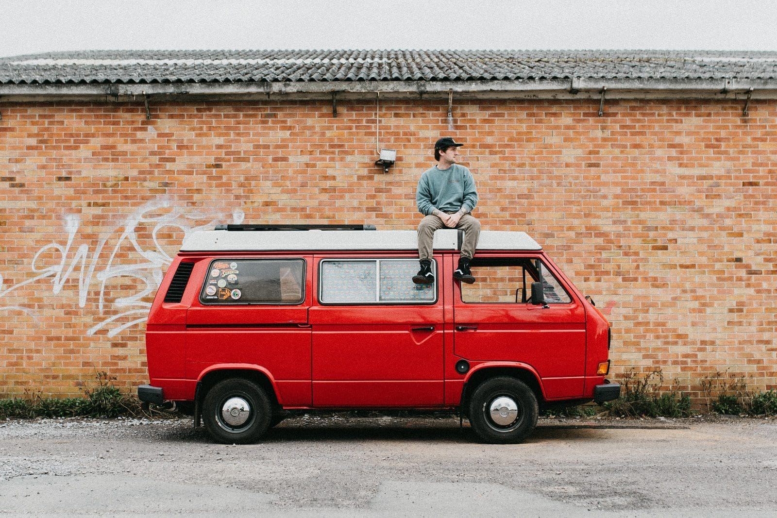 man in blue shirt and black pants standing beside red and white campervan