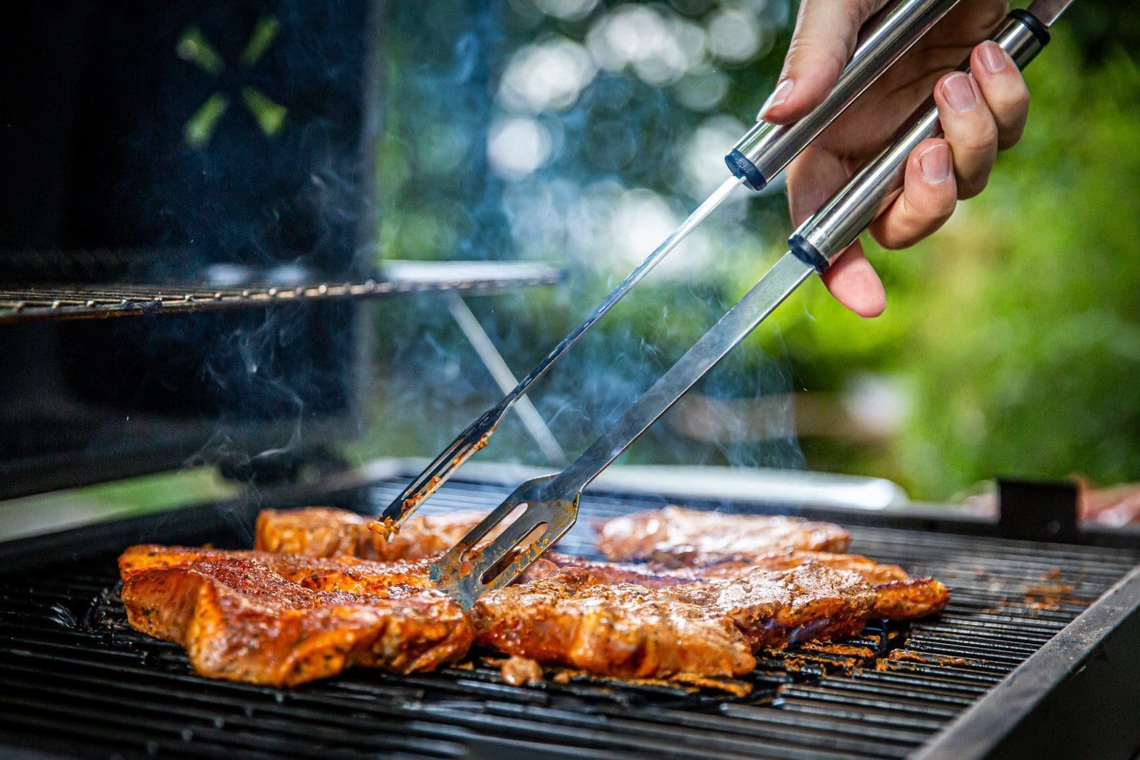charcoal fire person holding gray tongs on barbecue