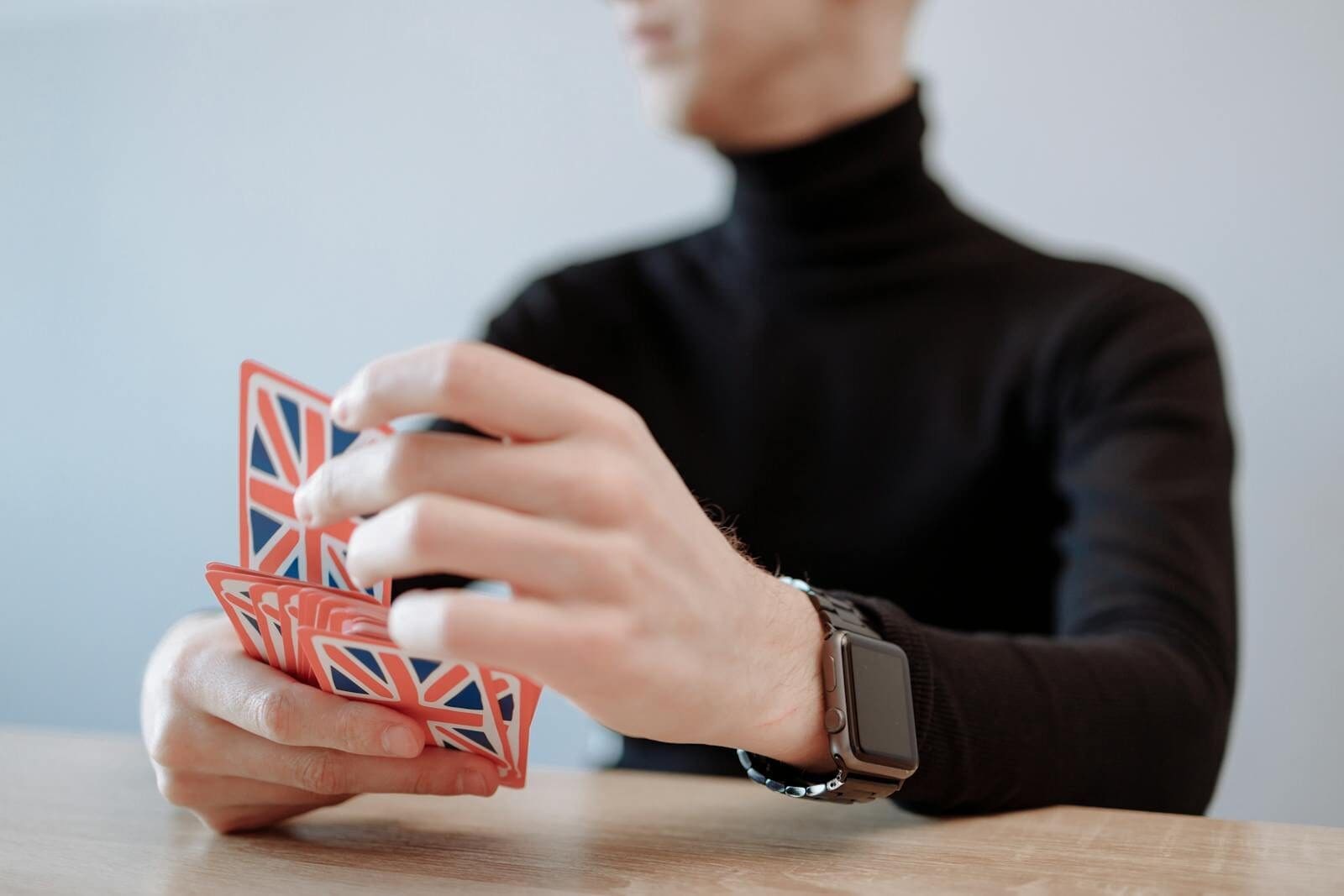 Close-up of a person with a smartwatch playing a card game with British flag cards. Focus on hands.